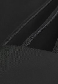 Černá tkanina s hladkým, strukturovaným povrchem s jemným žebrováním a kontrastním prošíváním. Měkké popruhy a čisté okraje pro minimalistický design.