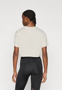 Κοντοκομμένο, ανοιχτό μπεζ μπλουζάκι με κοντά μανίκια. Απαλή υφή και στρογγυλή λαιμόκοψη. Συνδυάζεται με μαύρα κολάν με ψηλή μέση.