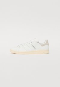 Zapatillas de cuero blancas con una pestaña de ante beige en el talón, diseño perforado en el lateral y suela de goma de color claro.