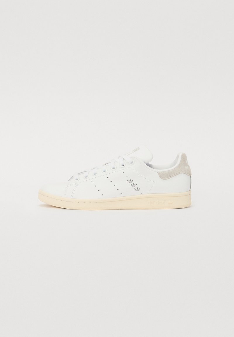 Zapatillas de cuero blancas con una pestaña de ante beige en el talón, diseño perforado en el lateral y suela de goma de color claro.