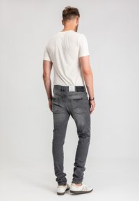 Szare jeansy denimowe o dopasowanym kroju, z tylnymi kieszeniami i białą metką na pasku, w połączeniu z gładkim białym t-shirtem i białymi butami.