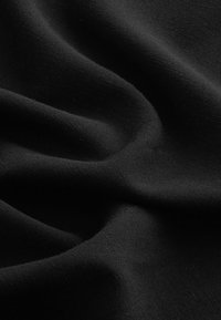 Le tissu noir présente une texture lisse avec un léger stretch et des détails de tissage, affichant une finition mate. Le matériau semble doux et flexible.