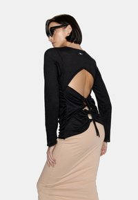 Czarna bluzka z długim rękawem o wyjątkowym designie z odkrytymi plecami, z marszczonym materiałem i detalami związującymi, w połączeniu z beżową dopasowaną spódnicą.