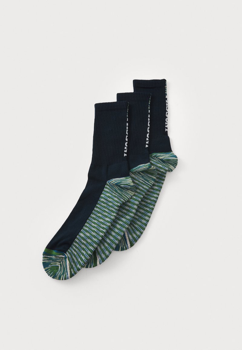 Tre par navy blå sokker med grønne, hvite og blå striped tær og hæler, lagt flatt og overlappende på en hvit bakgrunn.