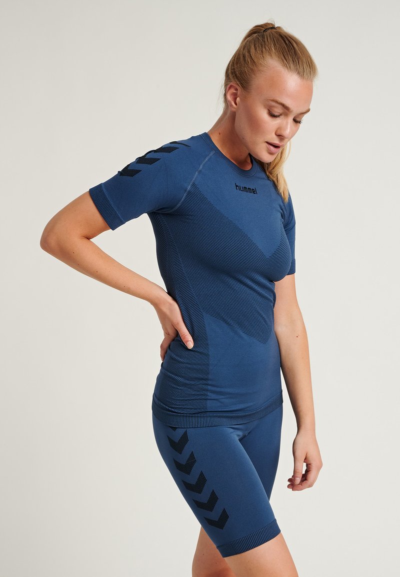 Ensemble de sport bleu marine comprenant un haut ajusté à manches courtes avec des panneaux texturés et un short assorti, rehaussé de motifs en chevrons noirs.