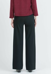Wide-leg black trousers with a smooth texture. Features a flat waistband and subtle creases. Paired with a maroon top, viewed from the back.
