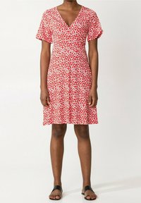 Robe portefeuille rouge à motifs floraux avec des manches courtes, dotée d'un corps ajusté, d'une jupe fluide et de motifs de fleurs blanches sur un fond vibrant.