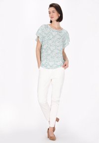 Lätt, blommönstrad blus i mintgrön, tillsammans med vita slim-fitbyxor och beige mockastövlar. Blusen har korta ärmar.