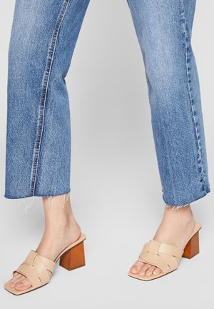 Beige læder mules med blokhæl og krydsede stropper. Parret med beskårede blå denim jeans med frynset kant og center søm.