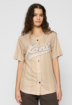 Beige Kurzarm-Jersey mit vertikalen weißen Streifen, Knopfverschluss und einem auffälligen Logo, auf dem "est. 1989" gedruckt ist.