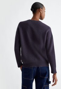 Maglione a maglia di un viola scuro, con una vestibilità rilassata, texture a coste e spalle cadenti, abbinato a pantaloni cargo in denim.