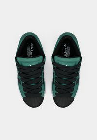 Πράσινα αθλητικά παπούτσια με μαύρα κορδόνια, ανάγλυφο σουέτ επάνω μέρος, καουτσούκ προστατευτικό στην άκρη και λευκή σόλα. Διαθέτουν λογότυπο στις εσωτερικές σόλες.