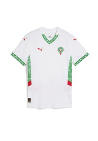 Camiseta de fútbol blanca con ribetes verdes en el diseño, logos rojos de Puma en las mangas y el pecho, y un escudo circular del equipo en el lado izquierdo del pecho.