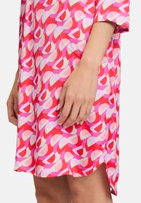 Baumwollkleid mit einem bunten abstrakten Muster in Rot, Pink und Creme. Verfügt über einen lässigen Schnitt, kurze Ärmel und seitliche Schlitze.