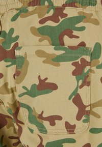 Beige maskáčové cargo šortky, s zadní kapsou, s abstraktními zelenými a hnědými tvary. Materiál je pevná bavlněná směs. S texturou.