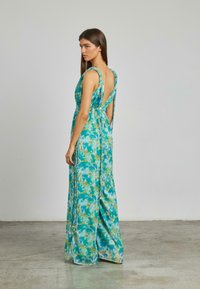 Długa, bezrękawna sukienka w kolorze turkusowym z kwiatowym wzorem. Posiada głęboki dekolt na plecach, plisowany dół i swobodną teksturę materiału.