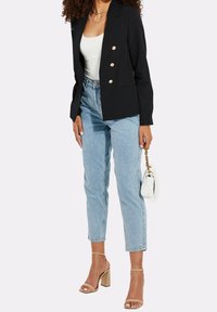 Blazer noir à double boutonnage avec des boutons dorés, associé à un jean taille haute bleu clair et des talons à lanières beiges. Petit sac à main blanc.