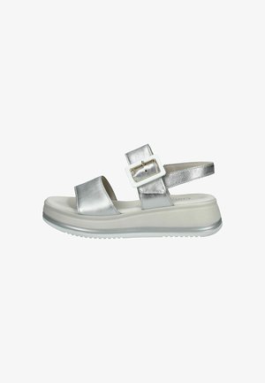 Sandalia metálica plateada con dos correas anchas, hebilla ajustable y una suela de plataforma blanca chunky con fondo texturizado.