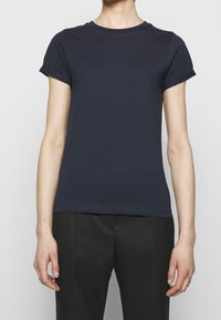 Marinblå t-shirt med kort ärm i slätt tyg, rund halsringning och uppvikt ärmslut, matchad med svarta skräddarsydda byxor.