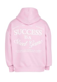 Felpa con cappuccio rosa chiaro con testo bianco sulla schiena: "Insegnato dalle strade, il successo è un gioco di strada," più una citazione motivazionale sottostante.