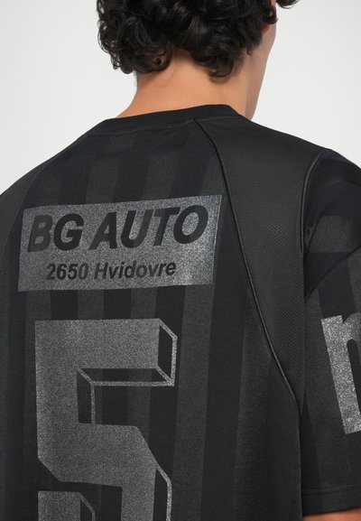 Črni športni dres z metalnimi srebrnimi napisi in grafiko, vključno z "BG AUTO" in "2650 Hvidovre," s teksturiranimi črtami.