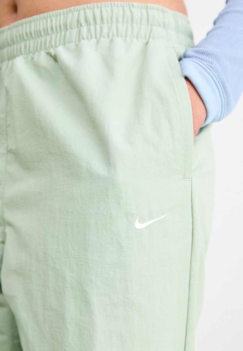 Pantalones deportivos de color verde claro con cintura elástica, que presentan un logo blanco de Nike en el bolsillo izquierdo y una tela suave y texturizada.