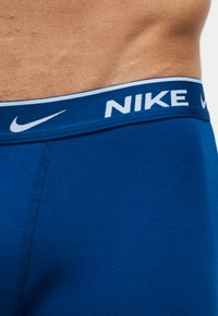 Μπλε ελαστική ζώνη εσωρούχου Nike στη μέση ενός ατόμου, που εμφανίζει το λογότυπο Nike και το swoosh στη λάστιχη ταινία.