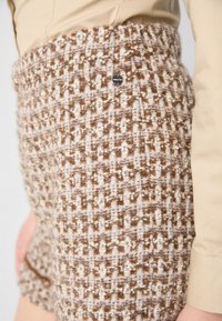 Wool blend shorts with a textured brown and cream check pattern, featuring a visible metal logo detail on the waistband.