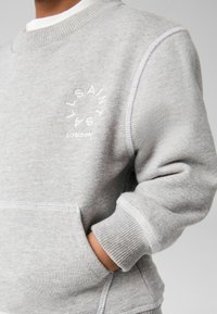 Šedá mikina vyrobená z mäkkej látky, s okrúhlym logom "SAINT LAURENT LONDON" nad prednou vreckom a rebrovanými manžetami.