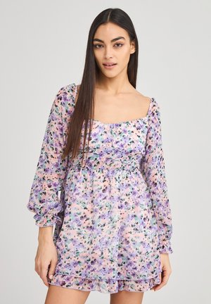 Abito floreale in colori pastello, con maniche a sbuffo lunghe, scollo quadrato e vita arricciata. Realizzato in tessuto leggero e trasparente.