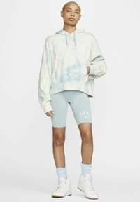 Gaiša krāsota kapuce krēmkrāsā un zilā, piparmētru zaļas velosipēdu šortos ar "NIKE" logo, baltas augstas kedas un zilas saspraudes zeķes.