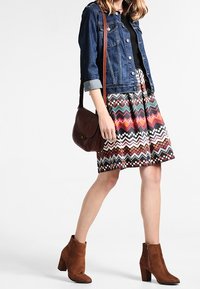 Jeansjacka, svart topp, mönstrad kjol med djärva chevrons och bruna ankelskor. En brun axelväska fulländar outfiten.