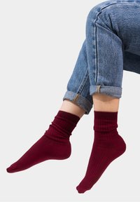 Burgundowe skarpetki prążkowane z podwiniętym mankietem, wykonane z miękkiego materiału, noszone z niebieskimi dżinsami z podwiniętymi nogawkami, charakteryzującymi się klasycznym krojem.