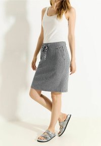 Jupe rayée noir et blanc avec une taille à cordon, longueur genou, associée à des sandales métalliques argentées. Texture de tissu lisse.