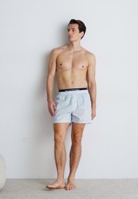 Boxeri bărbați cu dungi în albastru deschis, cu un elastic negru la talie, având o croială relaxată și un material moale din bumbac.