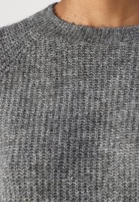 Pull en maille gris avec une texture côtelée et un col rond, fabriqué dans un matériau doux et léger, avec de subtiles variations de couleur.