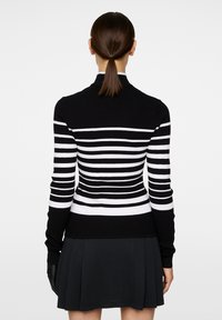 Svart och vit randig ribbad tröja med figurnära design, hög krage och långa ärmar. Passar bra med en svart utsvängd kjol.