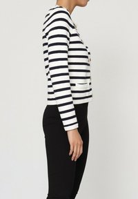 Cardigan rayé en blanc et bleu marine, avec des manches longues, un col rond, une fermeture à boutons, deux poches avant et un tissu tricoté texturé.