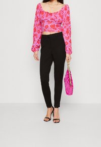Haut court à fleurs rose avec encolure froncée, pantalon noir ajusté, talons noirs à lanières et un sac matelassé rose vif avec chaîne dorée.