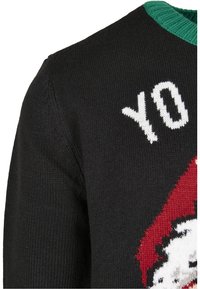 Pull en maille noire avec col vert, texte blanc "YO" et partie d'un visage de Père Noël rouge et blanc.