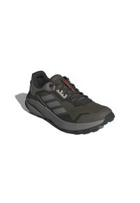 Chaussure de sport vert foncé avec un dessus texturé, des accents gris, trois bandes gris, et une semelle en caoutchouc noir. Présente des lacets rouges et un détail de logo.