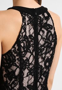 Schwarzer Spitzen-Bodysuit mit floralen Mustern, transparenter Textur und figurbetontem Design. Mit einem einfarbigen schwarzen Ausschnitt und einem Reißverschluss auf der Rückseite.