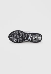 Såle av hvit sneaker med svart og hvit geometrisk mønster og en liten flerfarget logo i midten.