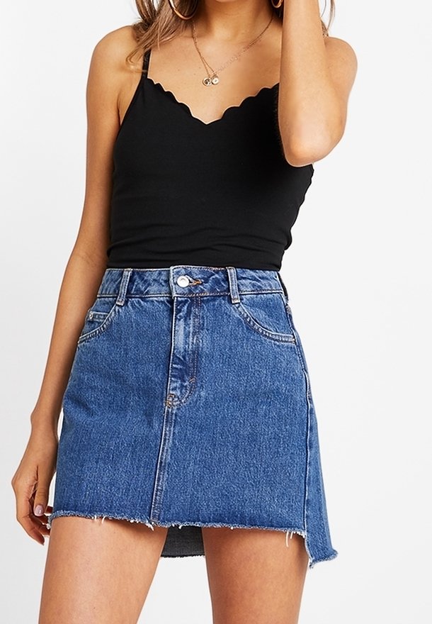 Woman wearing a black scalloped-edge tank top and a blue denim mini skirt with a raw hem and front button closure.