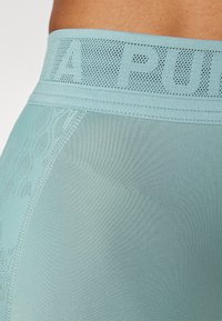 Leggings athletic di colore blu chiaro con una vita texturizzata e un logo. Il tessuto è liscio ed elastico, consentendo una facilità di movimento.