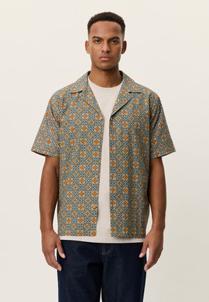 Kortærmet mønstret skjorte i blå, orange og cremefarver; har et gentagende blomster design og en camp-krave. Bæres over en lys t-shirt.