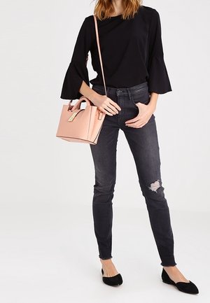Haut noir à manches cloche, jeans noirs déchirés, ballerines noires et un petit sac à main rose avec un détail de fermoir doré.