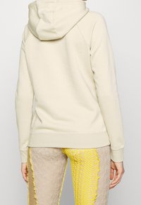 Beige hooded sweatshirt med avslappnad passform, med dragsko i huvan och ribbad mudd. Slät textur, enkel design, inga ytterligare dekorationer.