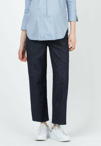 Los pantalones anchos de mezclilla oscura presentan una cintura alta y un corte recto, combinados con zapatillas blancas. La textura es suave con un ligero brillo.