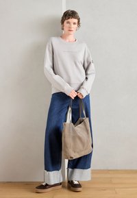 Lys grå sweatshirt med rund hals, kombinert med mørkeblå vide jeans med frayed hem. Brun suedetote bag og sko med hvite lisser.